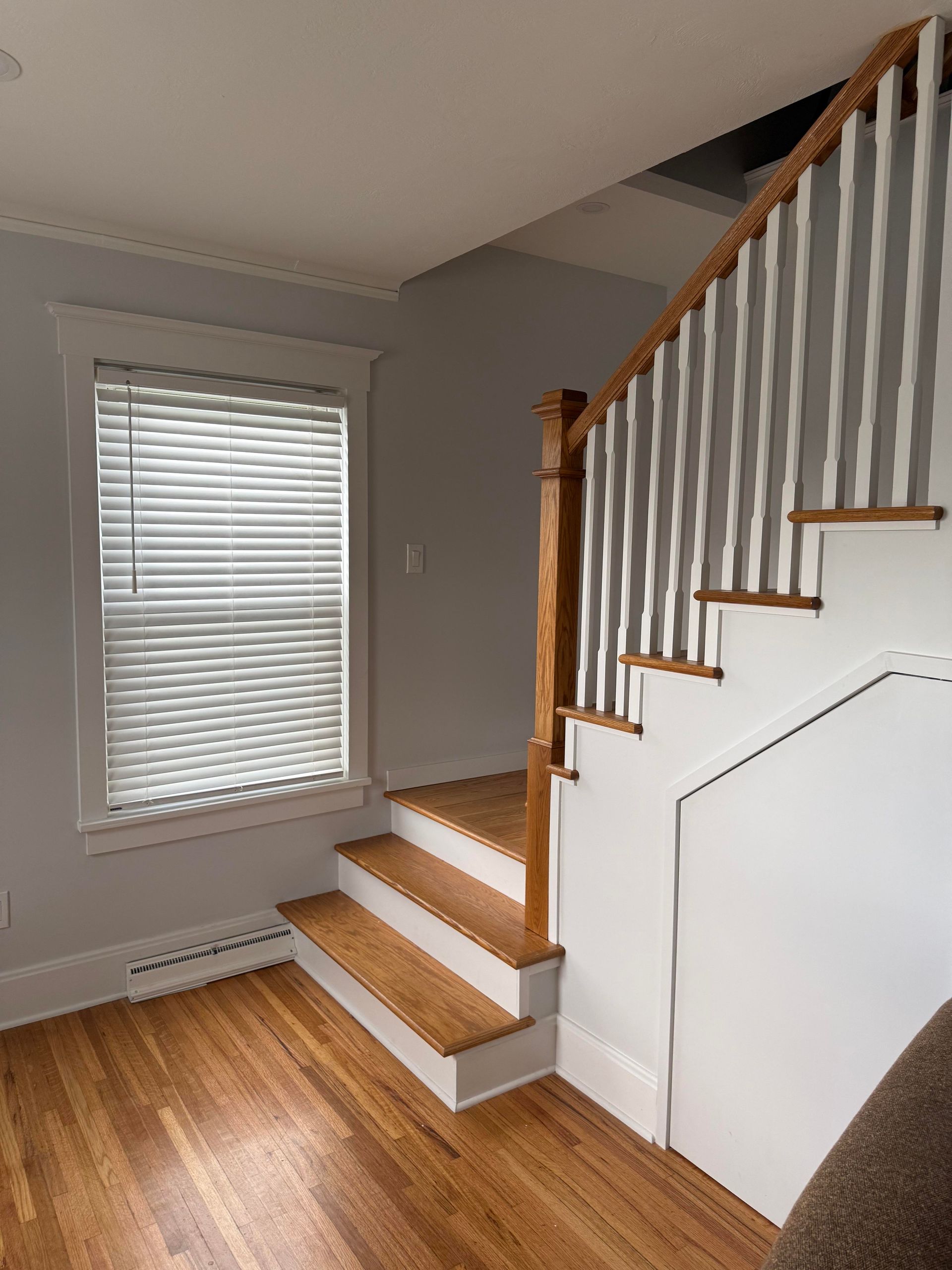 Interior staircase with wood steps, white railing, and a window in a small hallway