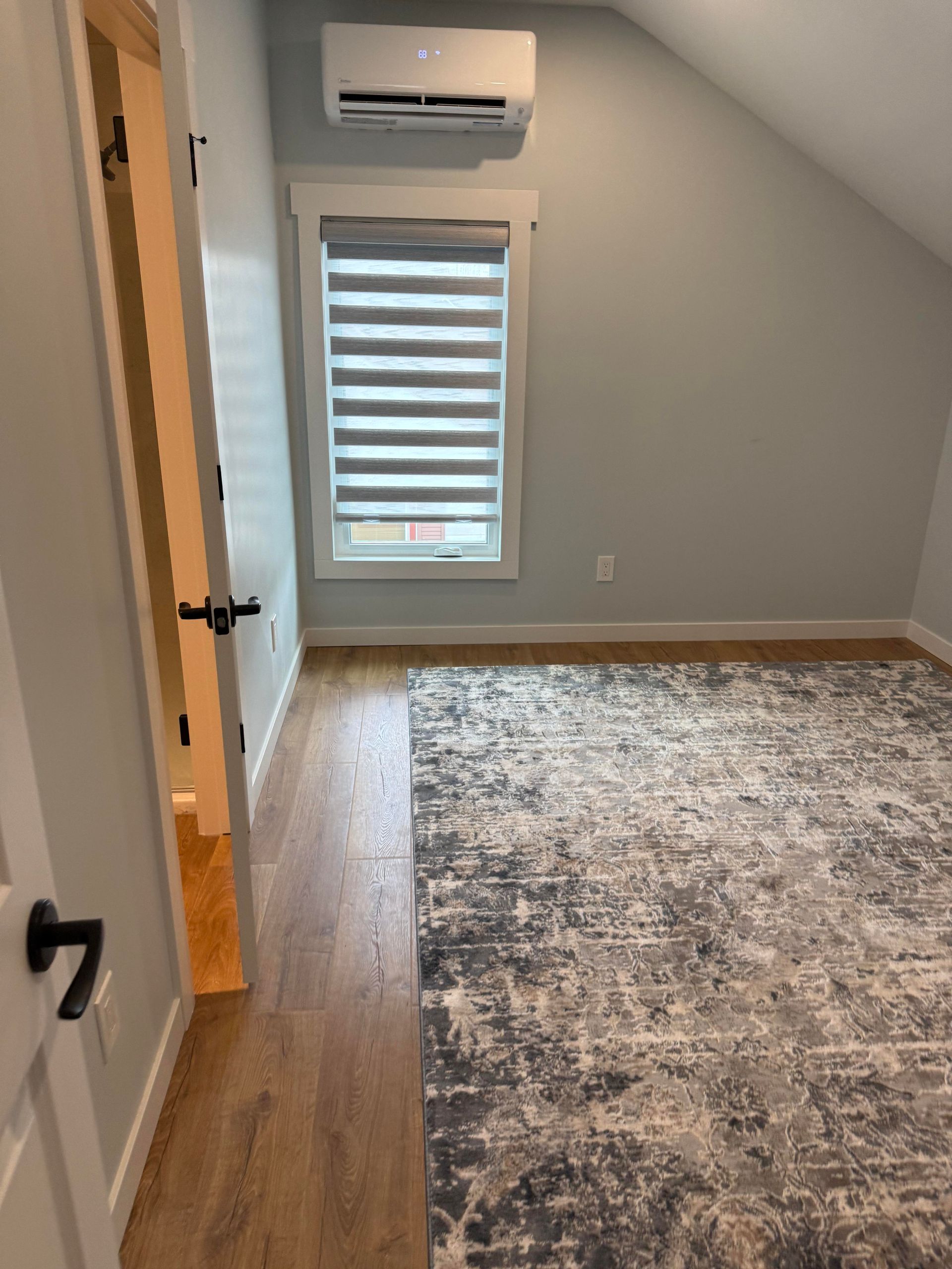 Empty attic bedroom with gray walls, window, wall AC unit, and large area rug