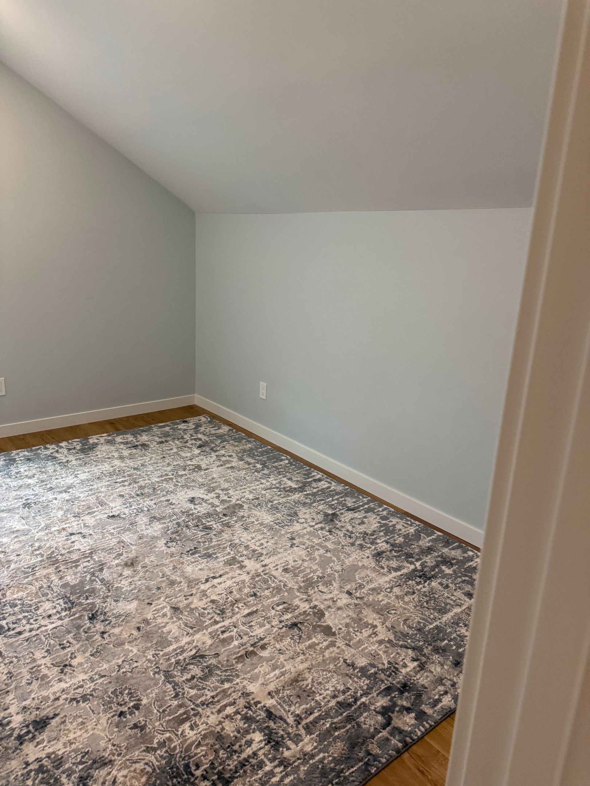 Empty carpeted room with gray walls, white trim, and a sloped ceiling.
