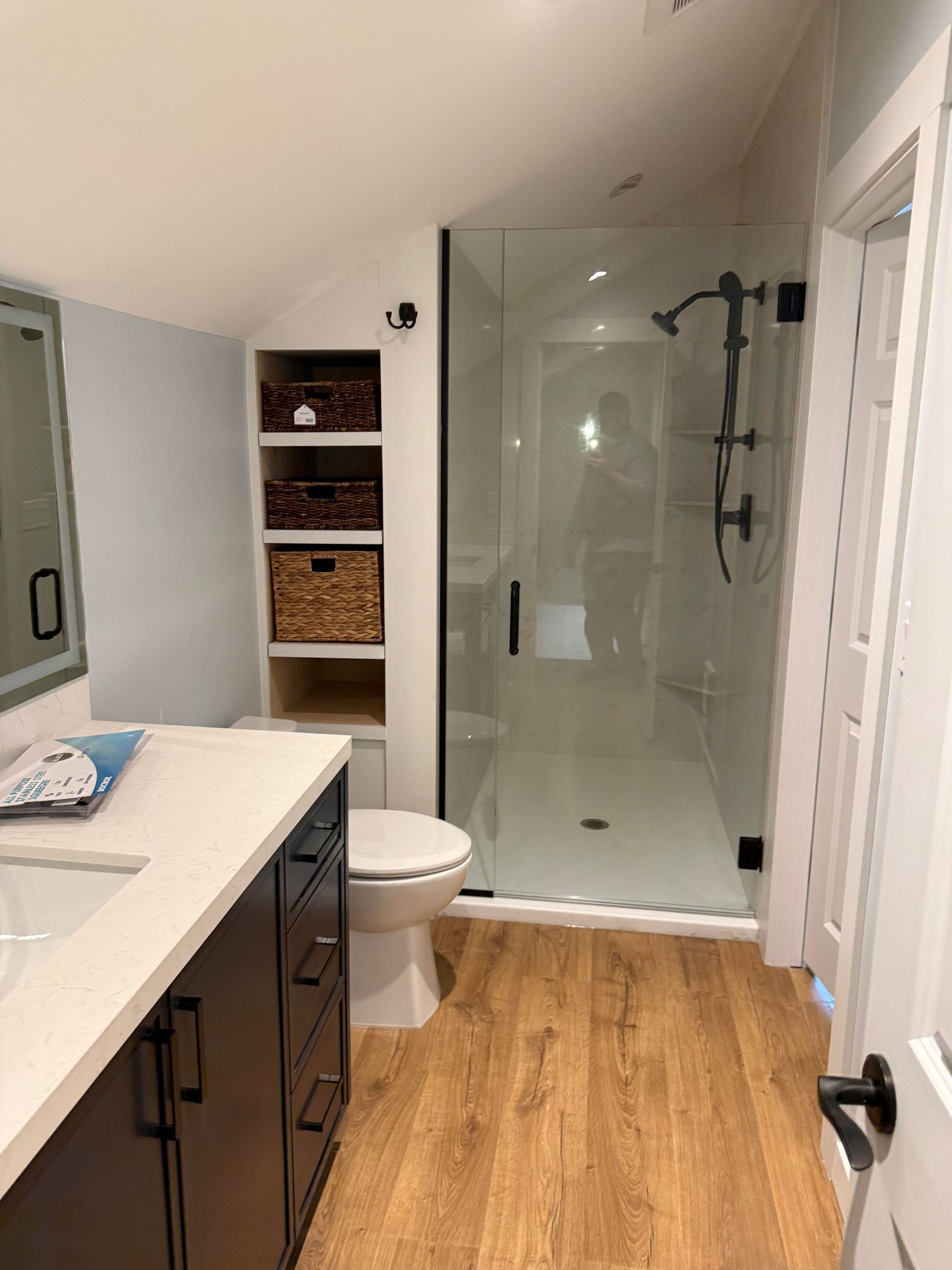 Modern bathroom with glass shower, vanity, toilet, and wicker shelves, seen from the doorway