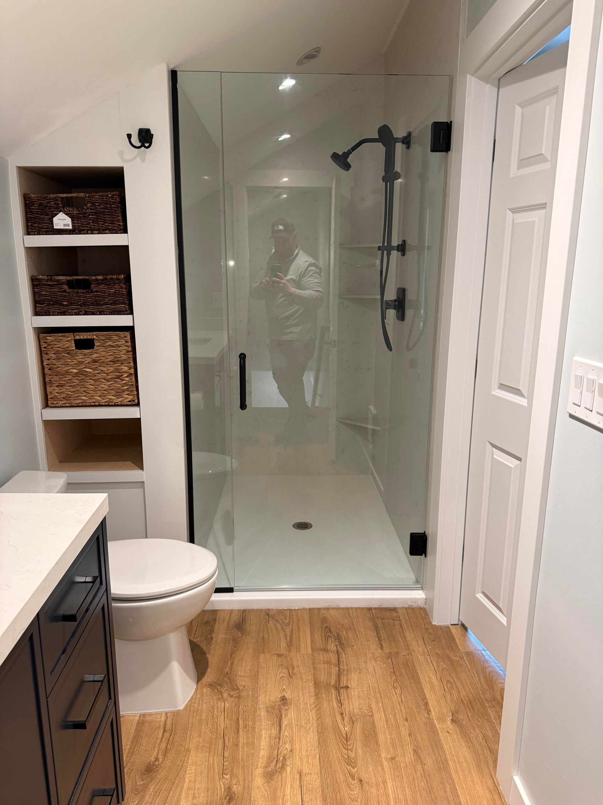 Bathroom with glass walk-in shower, wood floor, and white cabinetry with woven storage baskets.