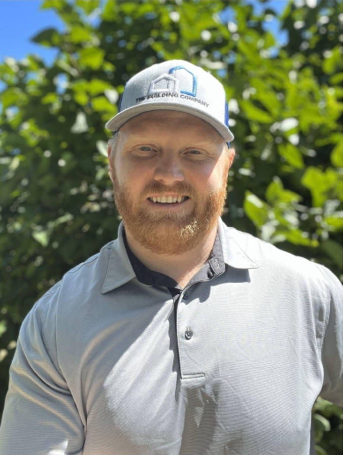 A man with a beard is wearing a hat and a grey shirt.