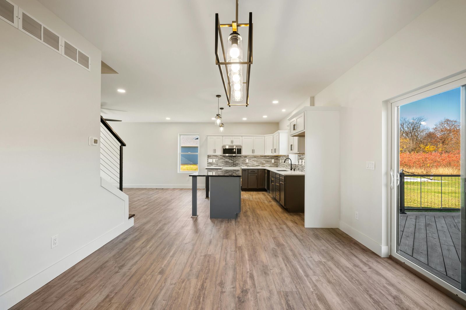 Bright open kitchen and dining area with wood floors, white walls, and a view to a deck and autumn trees.