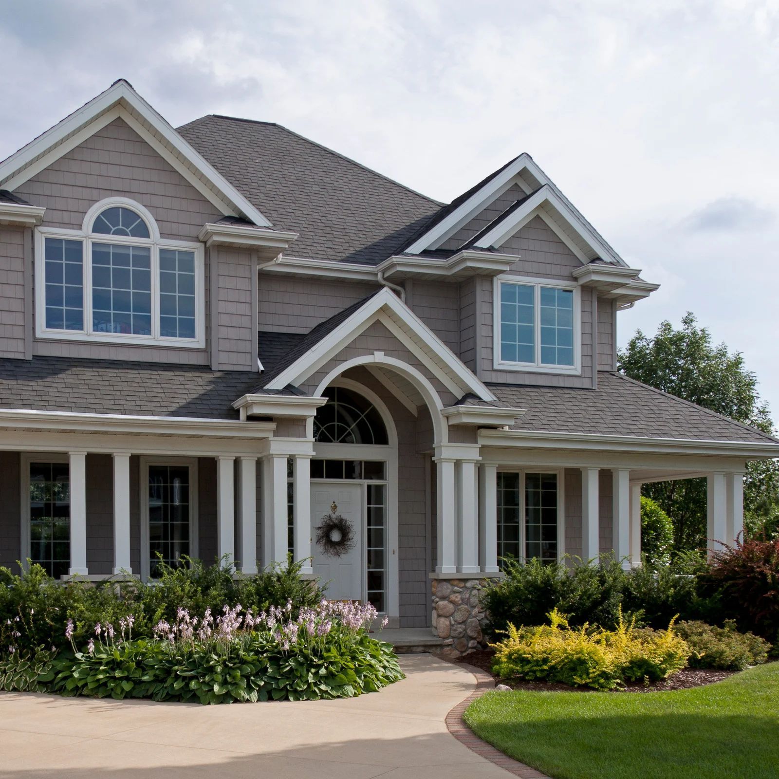 Two-story suburban house with gray siding, arched entry, front porch, and landscaped garden