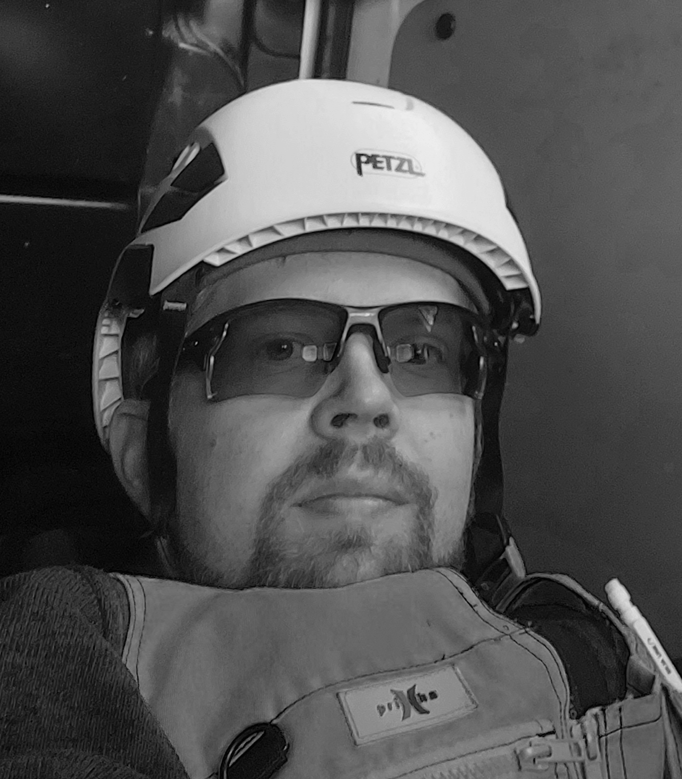 Mies, jolla on valkoinen Petzl-kypärä ja suojalasit, katsoo ylöspäin hämärässä ympäristössä