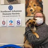 Woman holding a small dog beside a Northeast Arkansas Humane Society sign and pet count display (028)