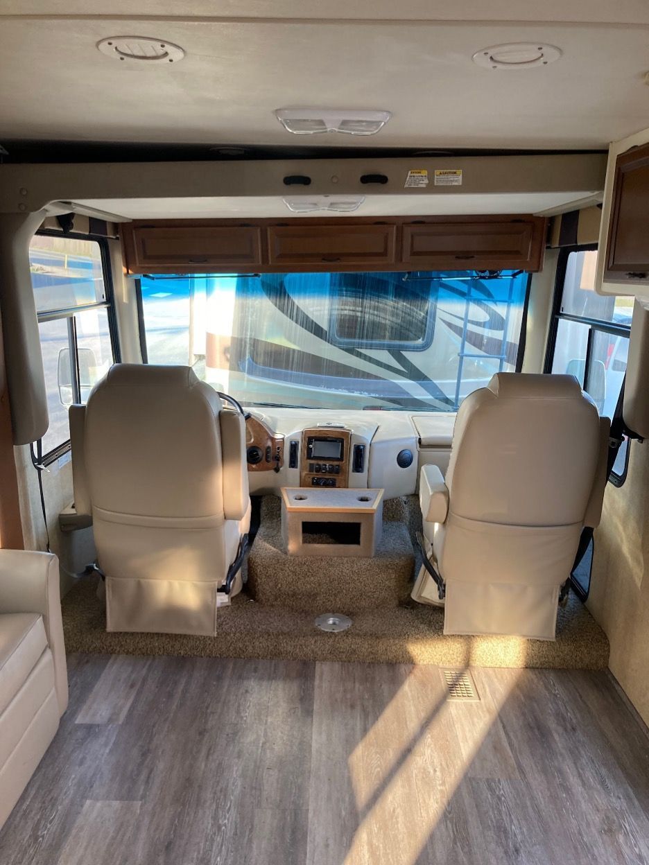 Interior view of a motorhome with beige captain's chairs, dashboard, and large windshield.