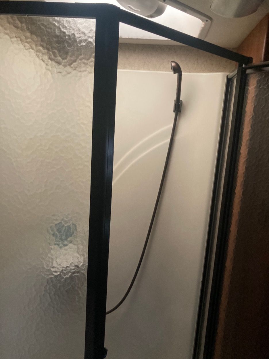 Shower stall in RV with frosted glass door, black frame, and handheld showerhead.