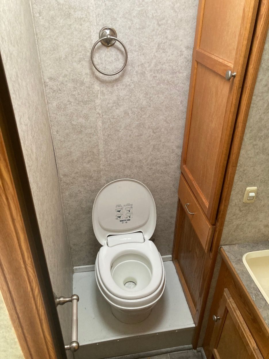 RV bathroom with toilet, towel ring, and storage cabinet. Gray floor and walls, wood trim.
