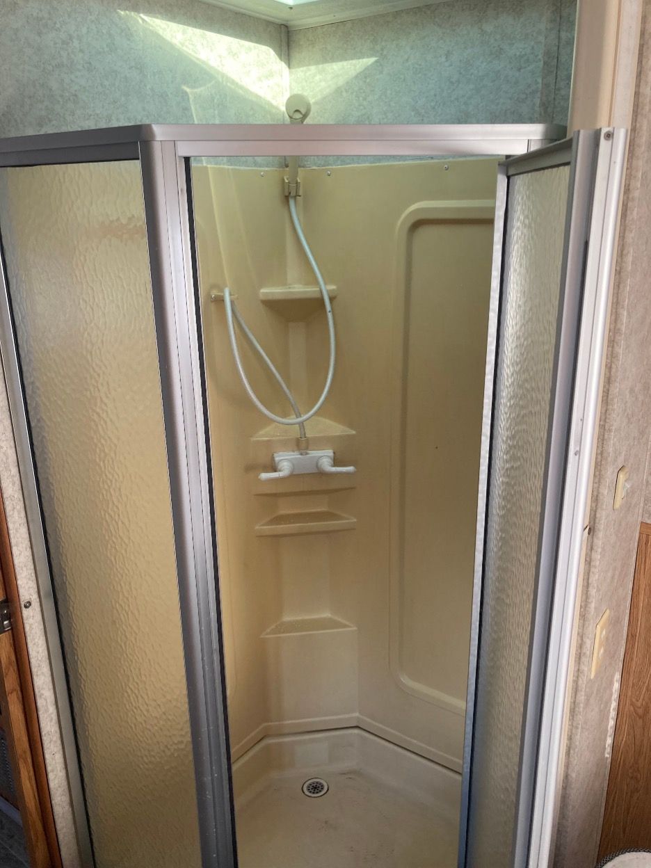A tan, corner shower stall with glass doors and a handheld shower head, inside a trailer.