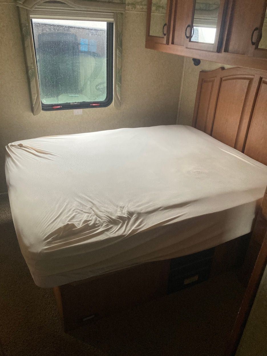 Bedroom in RV with queen bed, window, and wood cabinetry.