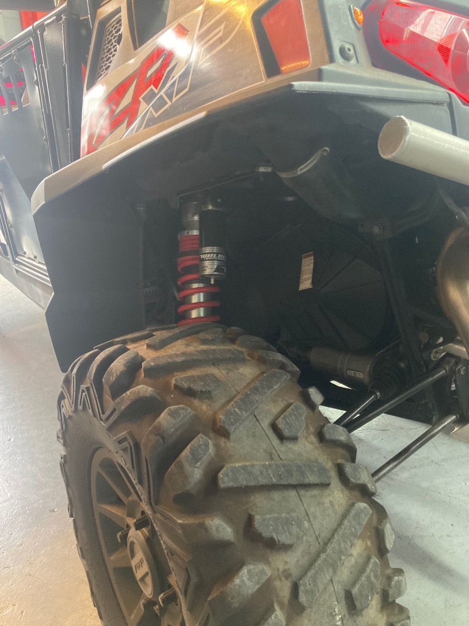 Black and red side-by-side UTV tire and suspension detail. Red shock absorber, black tire with visible tread.