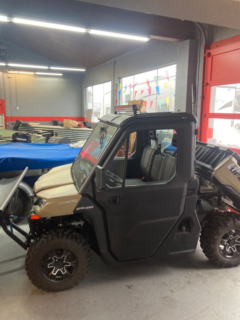 Tan and black side-by-side UTV in a garage, with a windshield, doors, and roll cage.