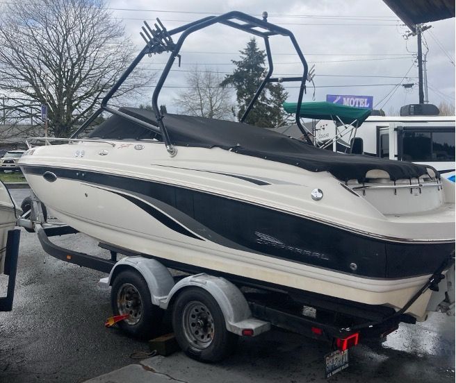 Boat on trailer, black and white color scheme, black wakeboard tower, overcast outdoor setting.