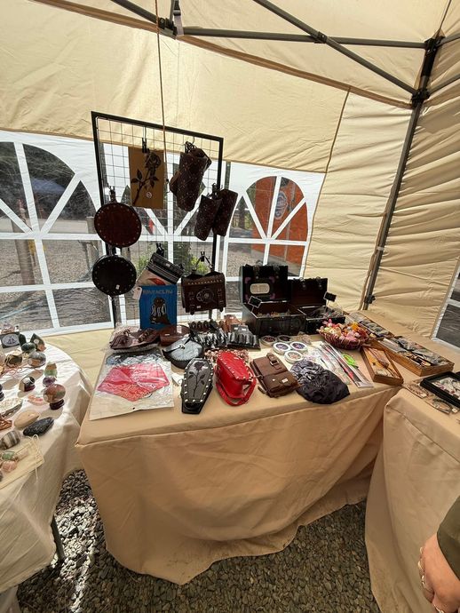 Market table under a tent displaying handmade jewelry and small crafts on a beige cloth-covered table