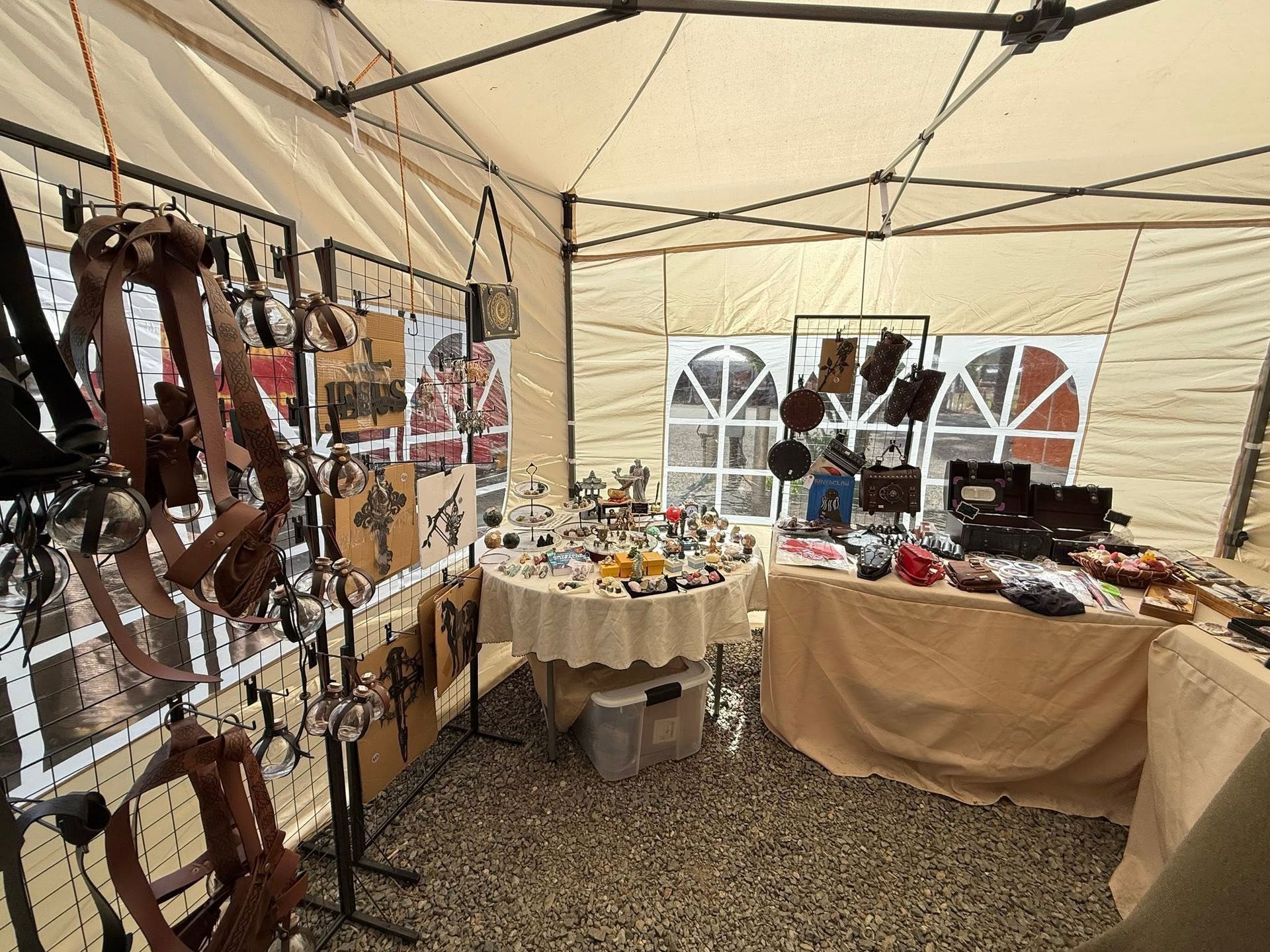 Market stall inside a tent displaying leather belts, jewelry, and small goods on tables