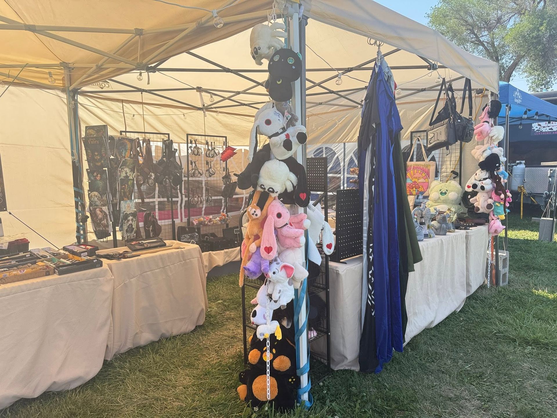 Outdoor market stall with hanging plush toys and clothes under a beige canopy