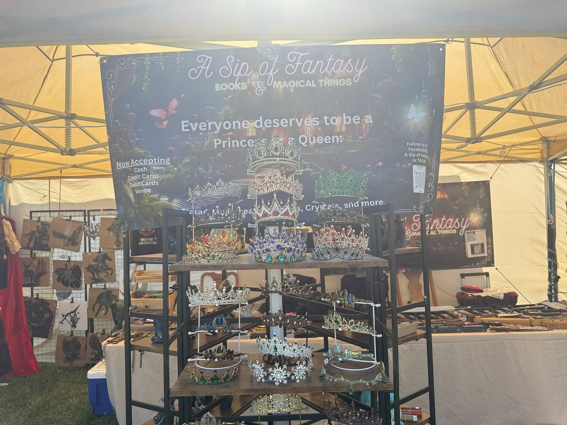 Black display booth at an outdoor market with pottery, plants, and a handwritten sign.