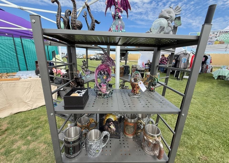 Outdoor market display of metal and glass sculptures on a black shelving unit under a colorful canopy