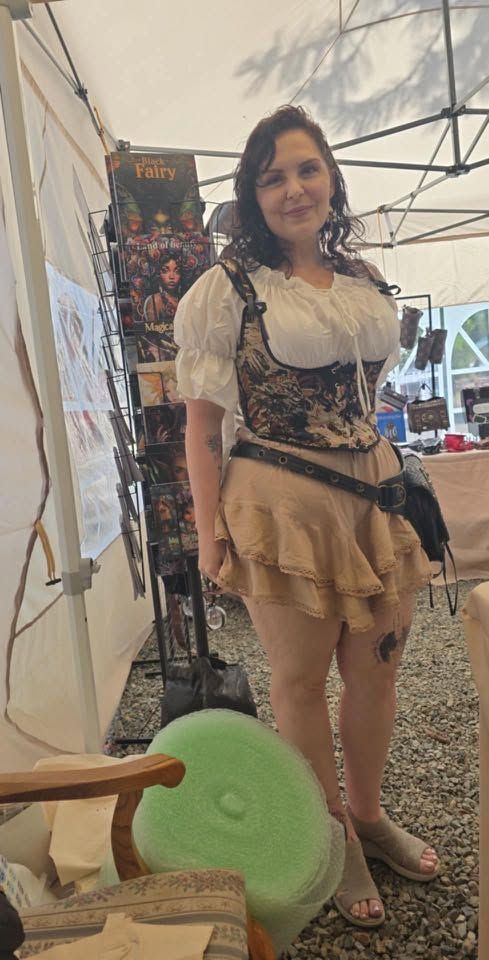 Woman standing in a tent, wearing a white top and beige skirt, smiling beside a green chair.