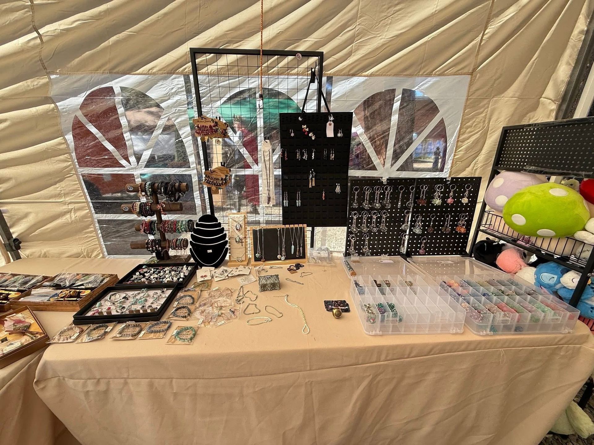 Vendor booth table with handmade jewelry displays, black stands, and colorful items under a tent