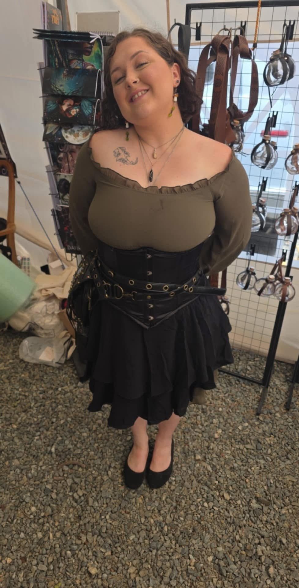 Woman standing in a shop, wearing a black skirt and green top, smiling at the camera.