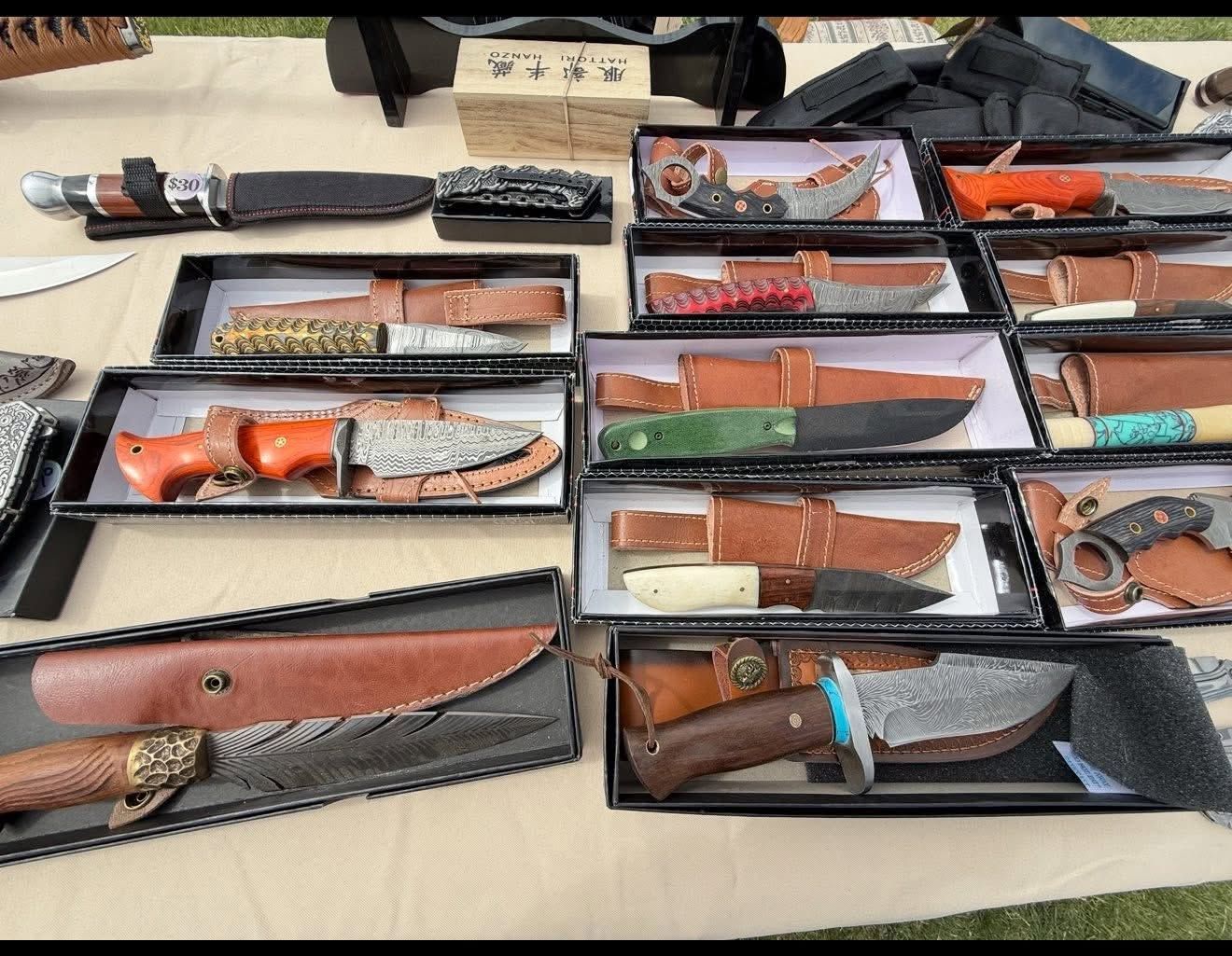 Assorted knives and sheaths displayed in open cases on a table indoors