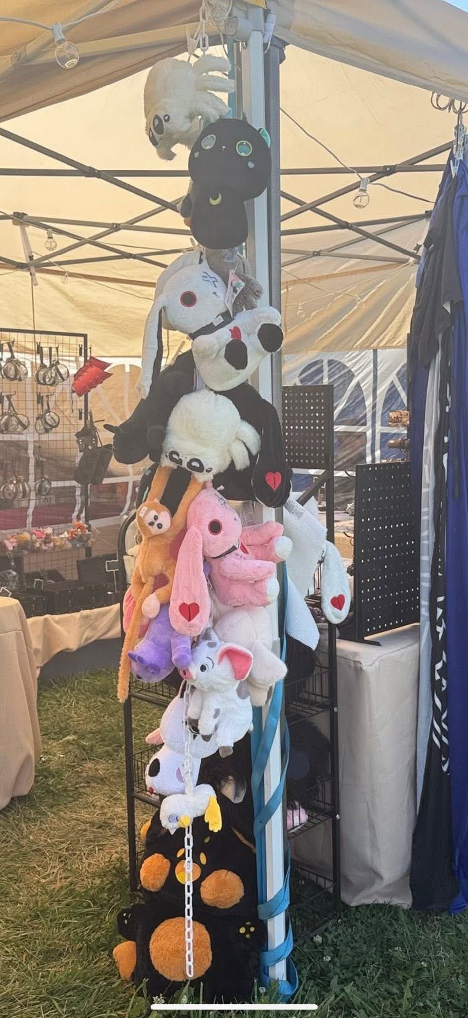 Hanging stuffed animal toys displayed on a black pole under a tent at an outdoor market.