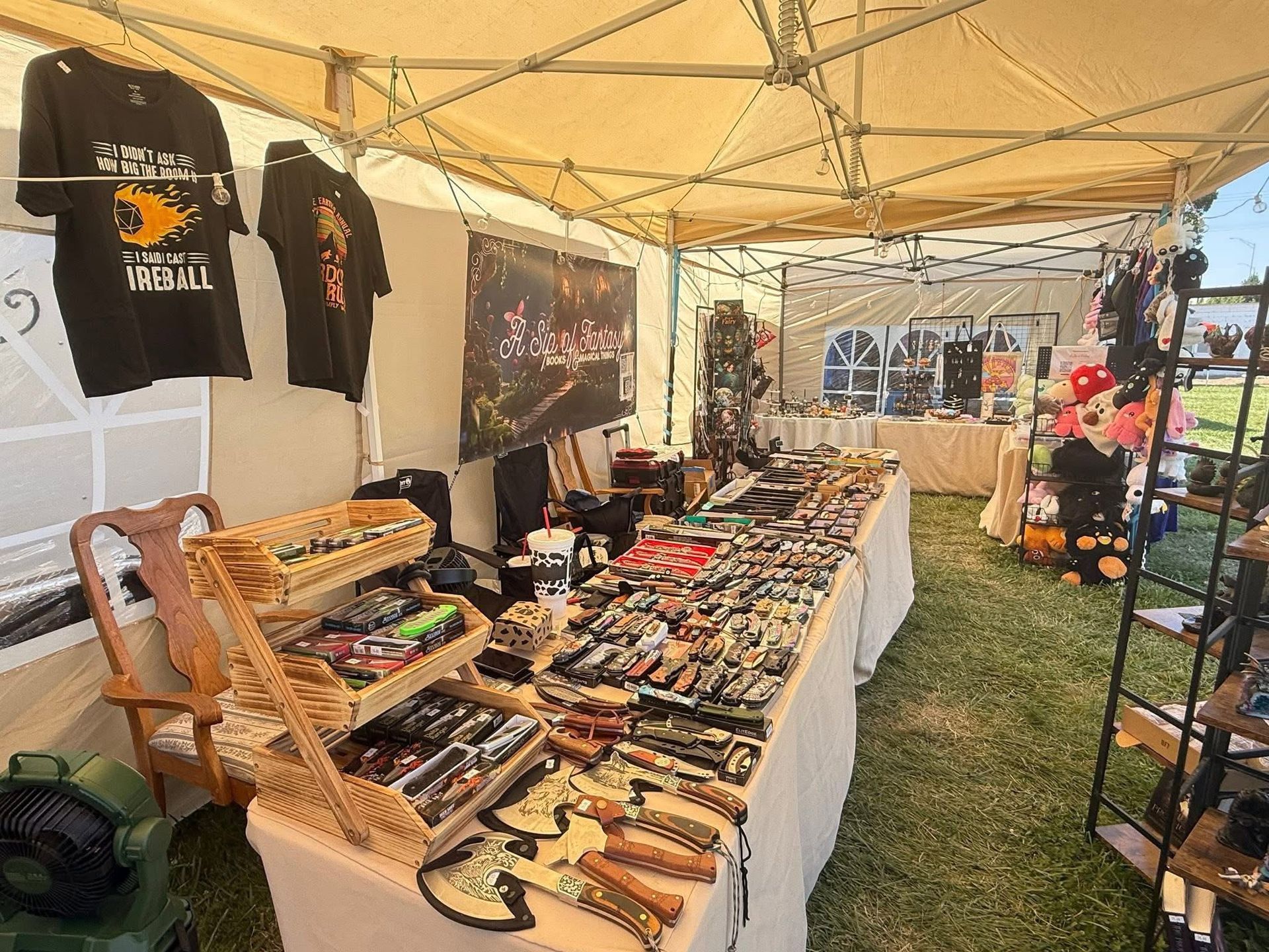 Outdoor market stall with knives and tools displayed on tables under a beige canopy