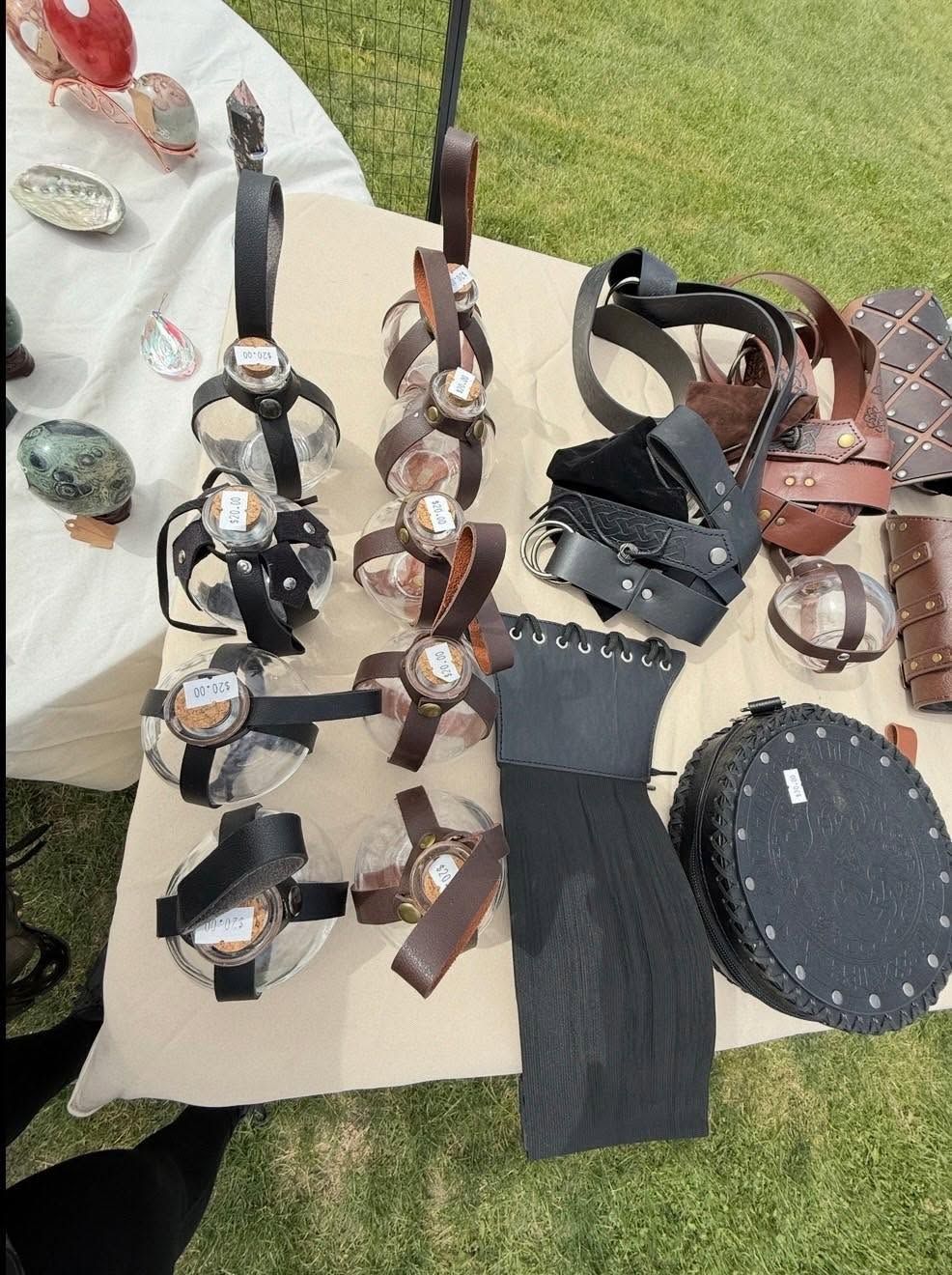 Assorted leather sandals and accessories displayed on a table outdoors on grass.