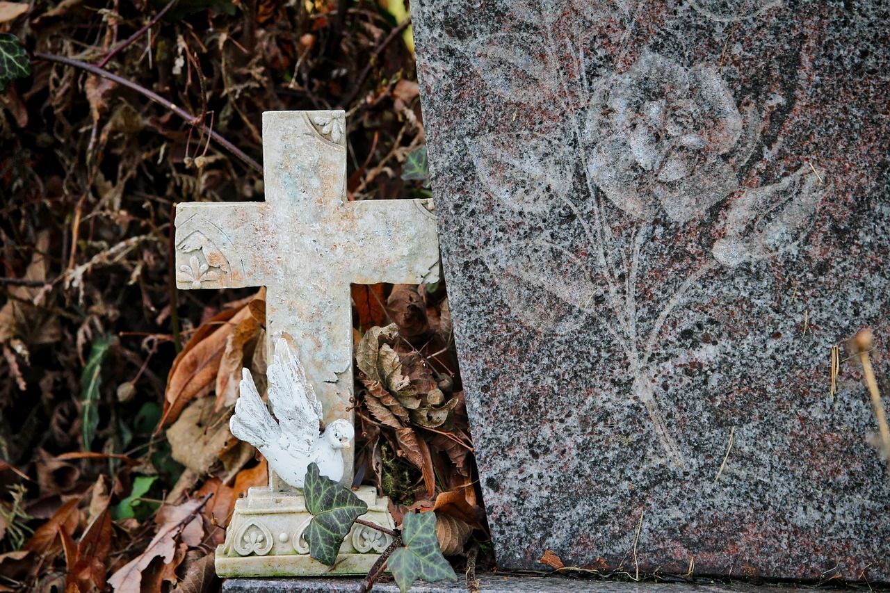 Picture of a cross headstone, next to a stone headstone, with a rose engraved on it