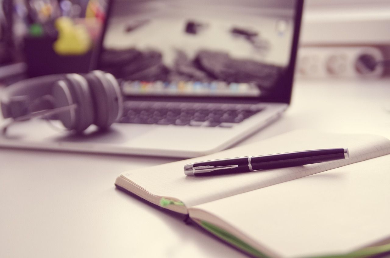 Image of a desk with a computer, notebook, and earphones
