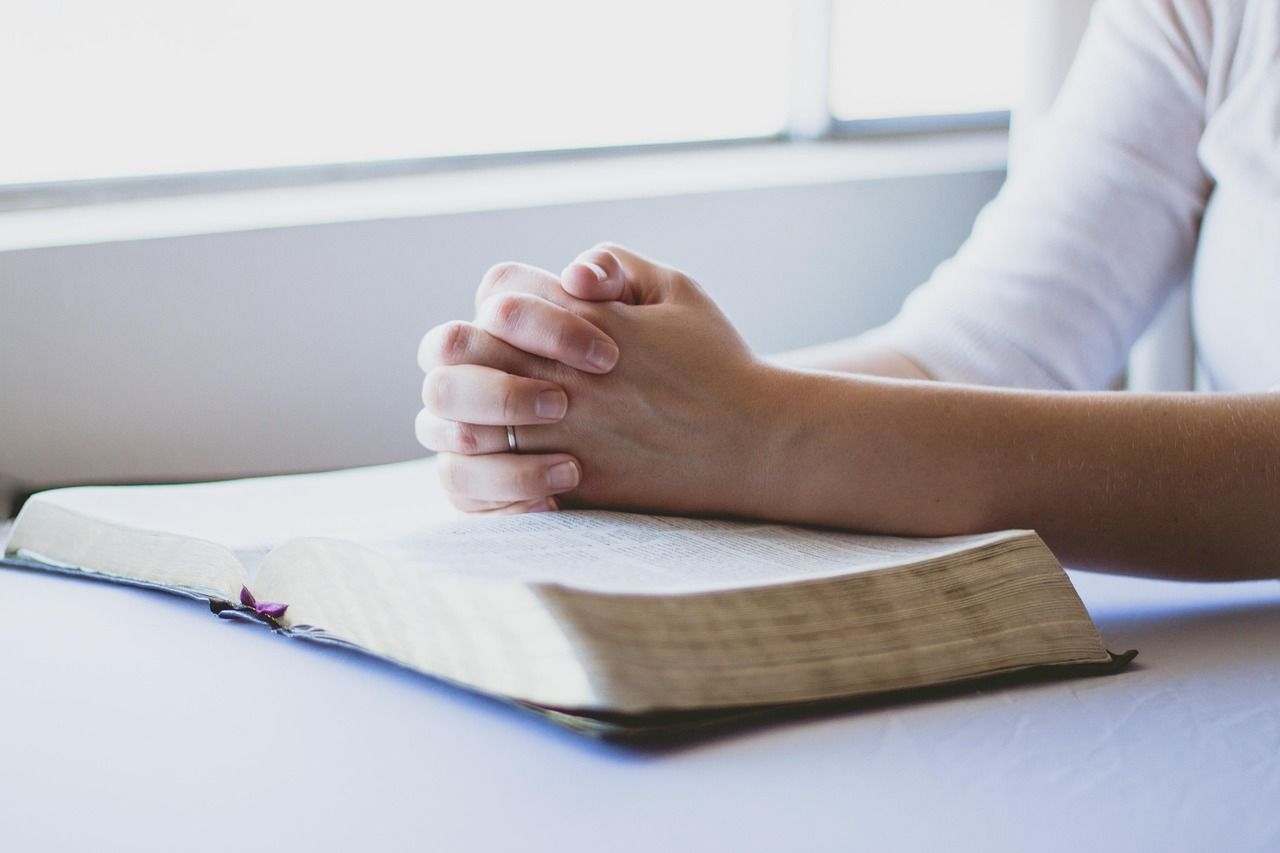 Photo of a person with their arms resting over an open book, wearing white clothes, on a white table