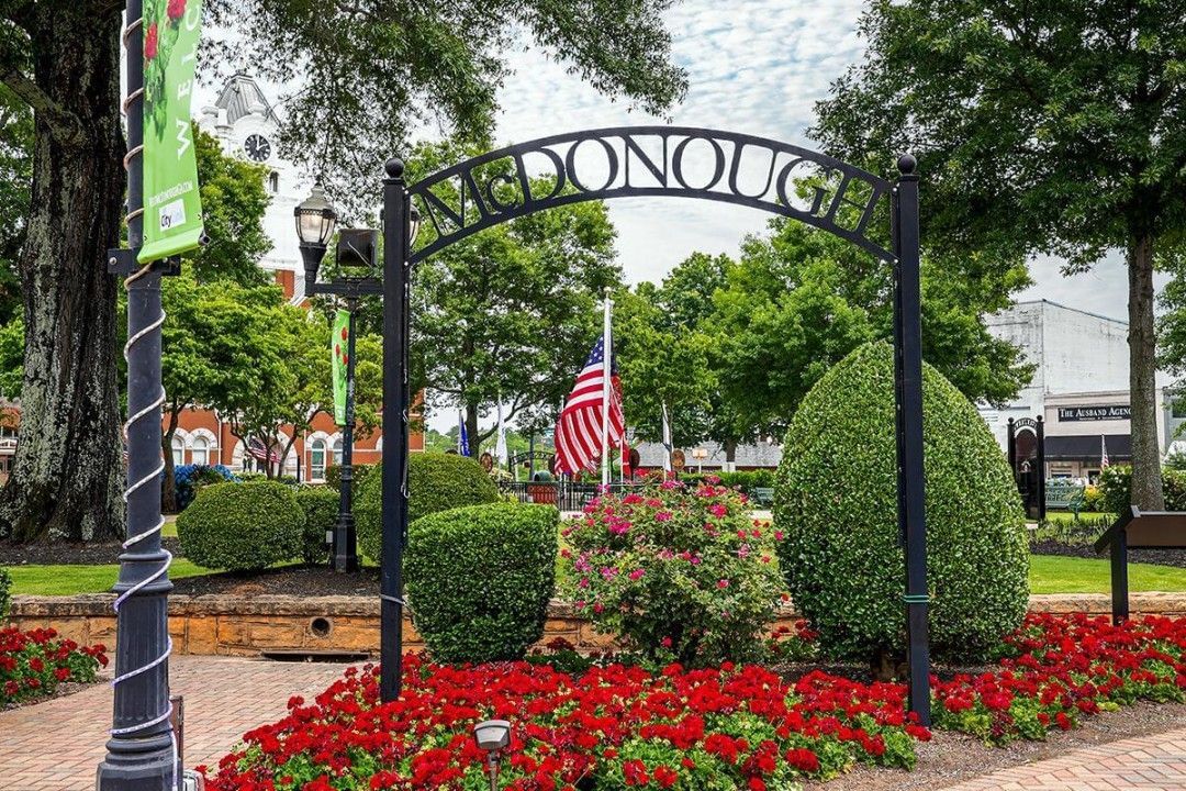 A sign in a park with red flowers and a flag in McDonough Ga