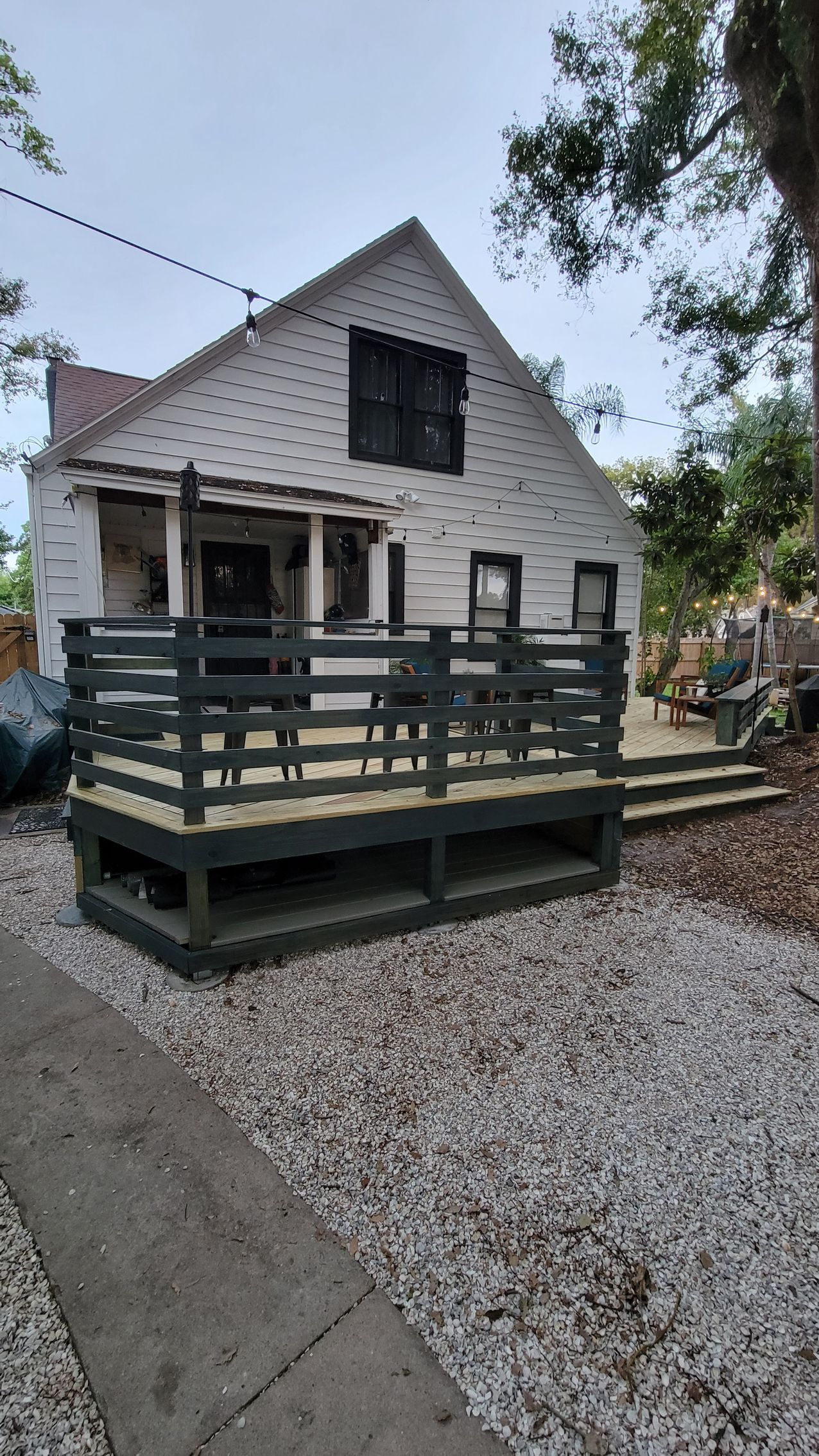 White house with black-trim window and green deck beside a gravel path and trees