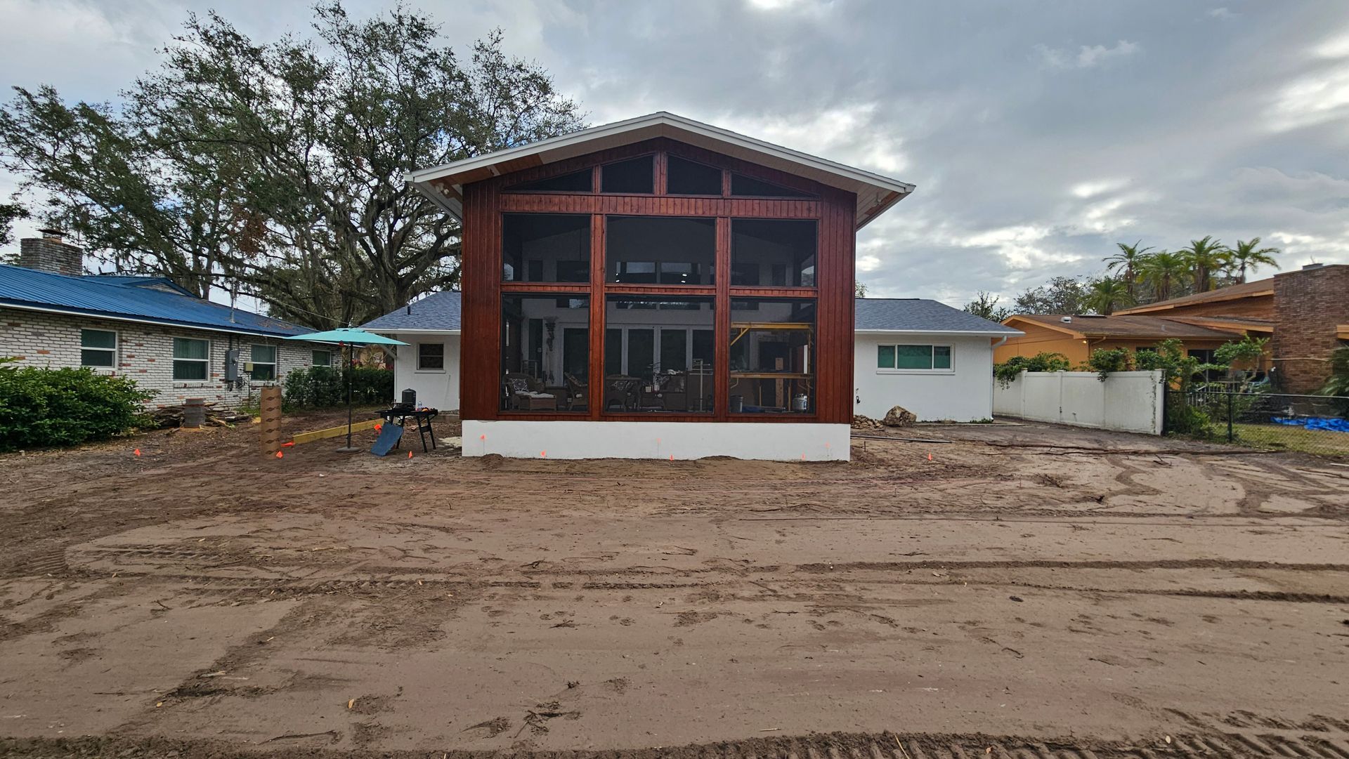 Small modern house with large red-framed windows on a muddy roadside under cloudy skies