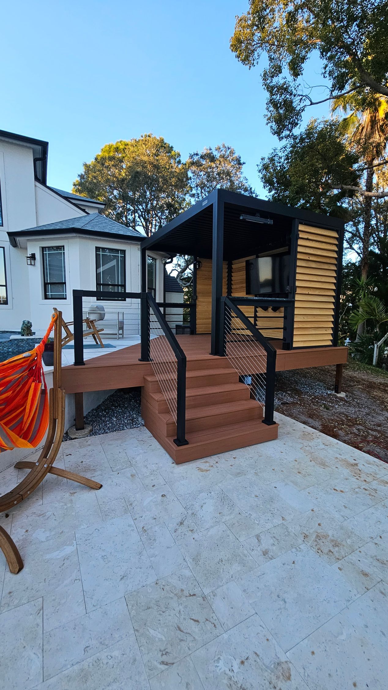 Wooden accessibility ramp and steps leading to a small black-and-wood house entrance outdoors.