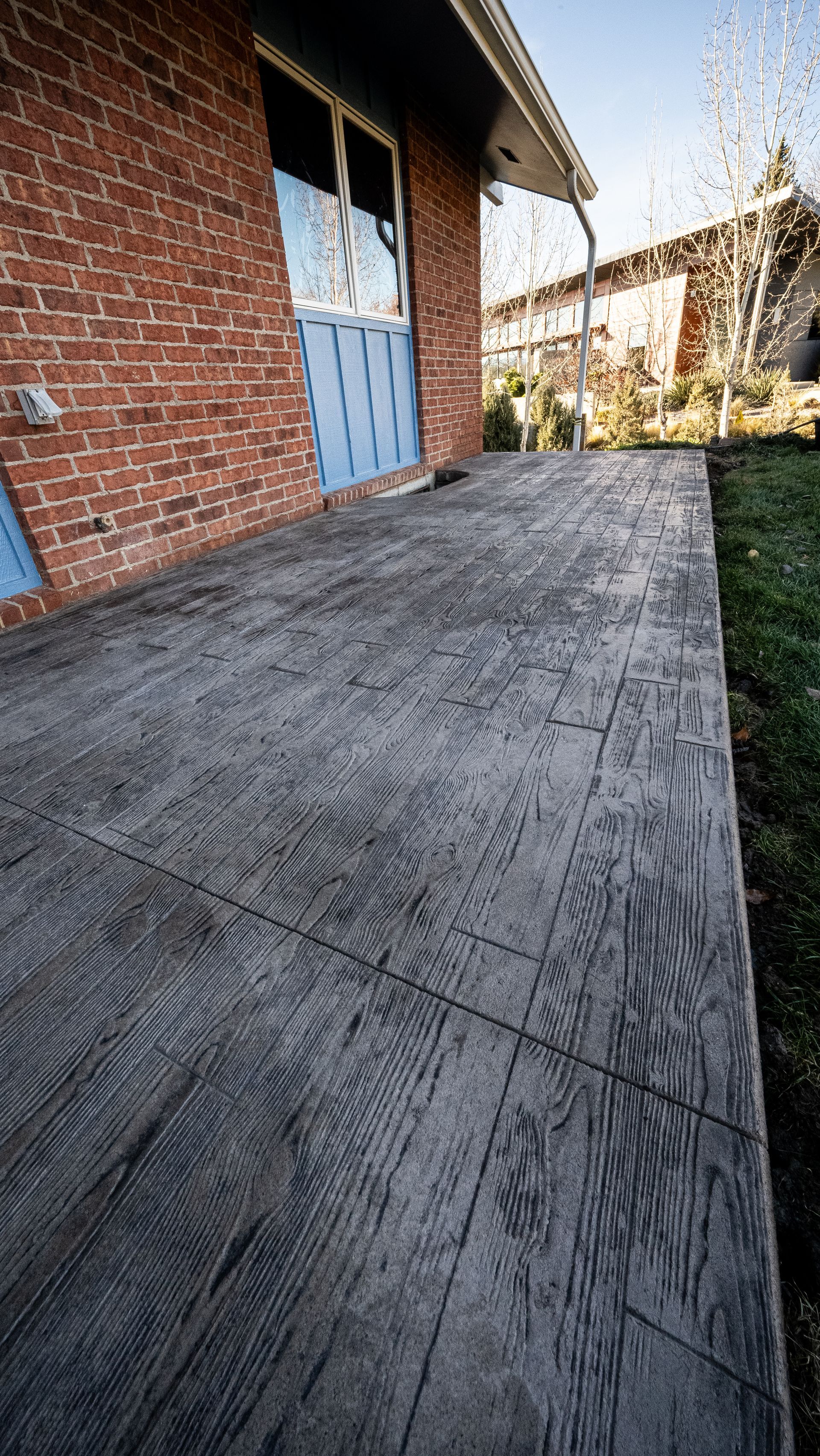 Concrete patio beside a brick house with blue doors and a hedge along the edge.