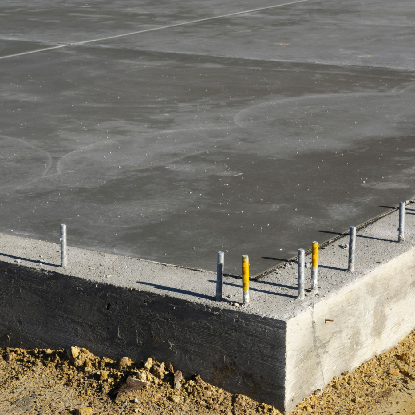 Concrete foundation slab with rebar rods protruding at the corner on a construction site
