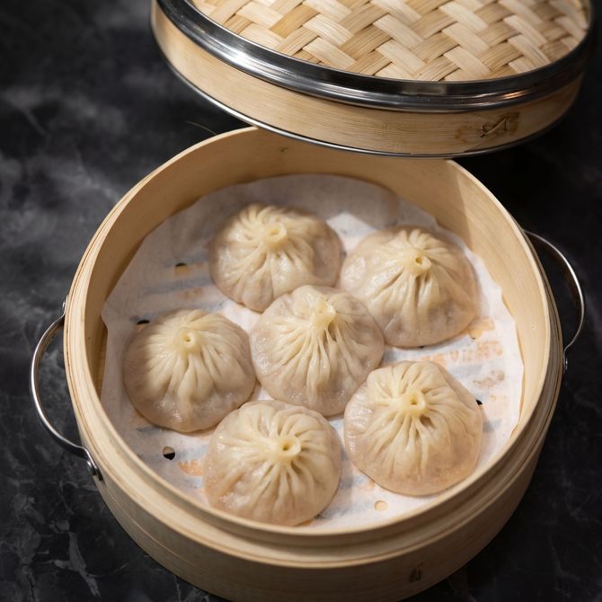 Bamboo steamer with six steamed dumplings on parchment paper