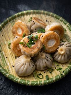 Assorted steamed dumplings and fried rings on a green leaf-patterned plate, garnished with herbs.