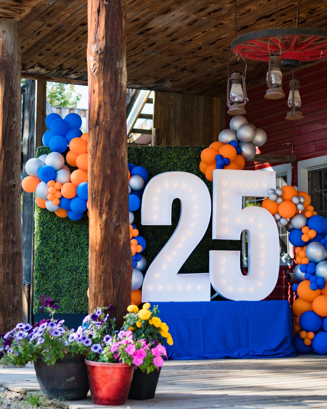 Decorated event display with large white “25” balloon numbers and blue, orange, and white balloon clusters on a stage