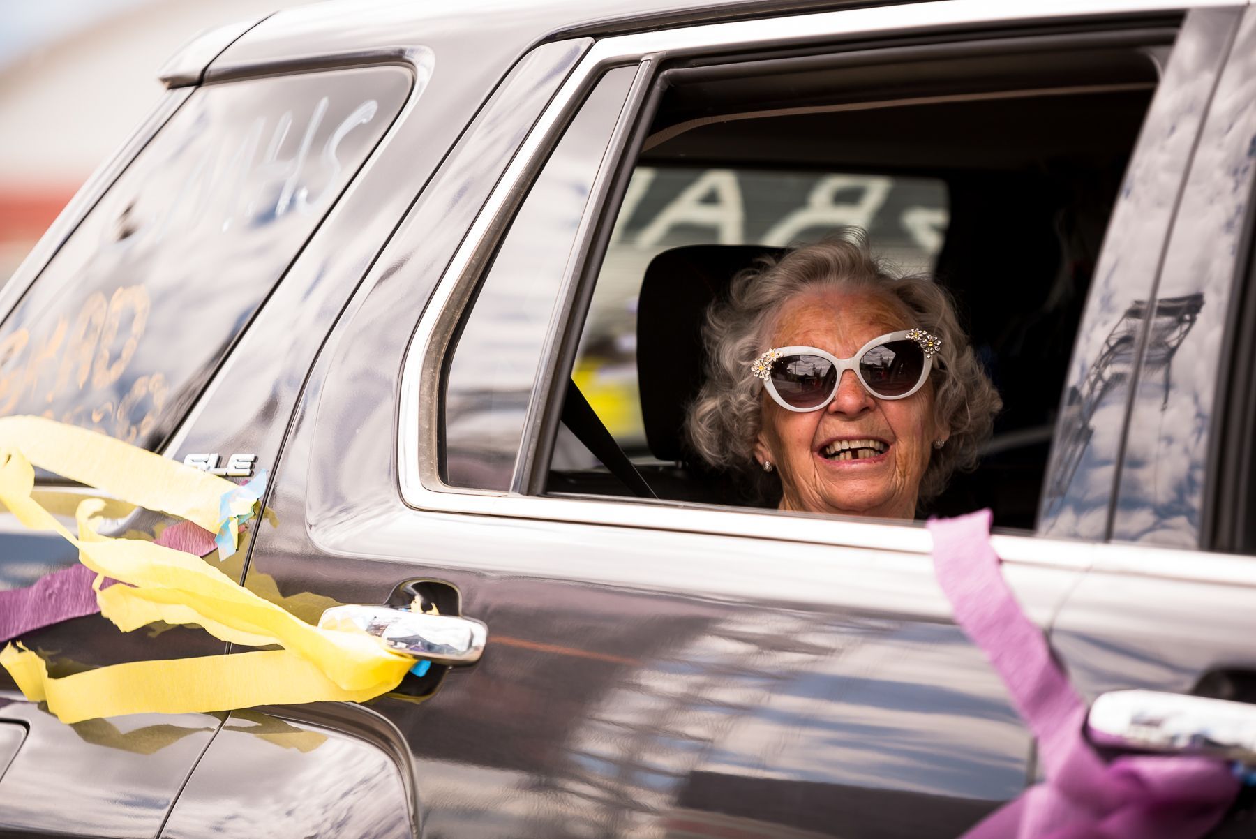 An elderly woman wearing sunglasses is sitting in a car.