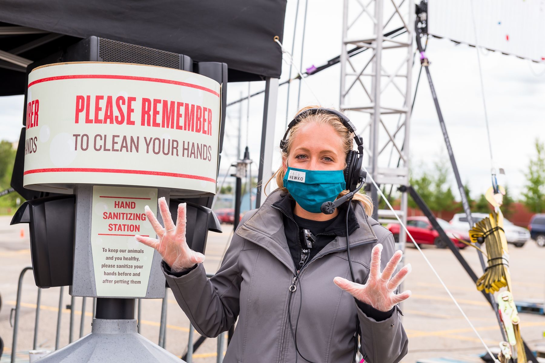 A woman wearing a mask and gloves is standing in front of a machine that says please remember to clean your hands.