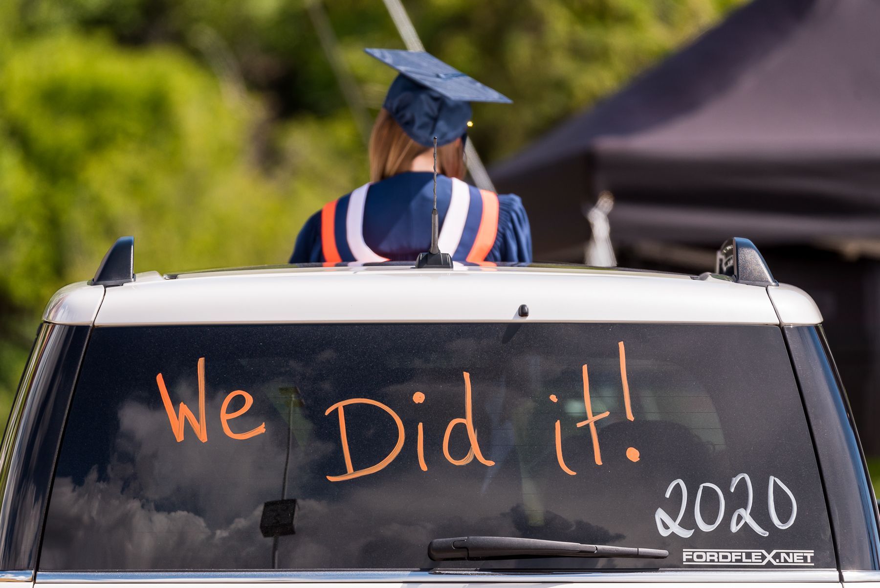 A woman in a graduation cap and gown is sitting in a car with the words we did it written on the back window