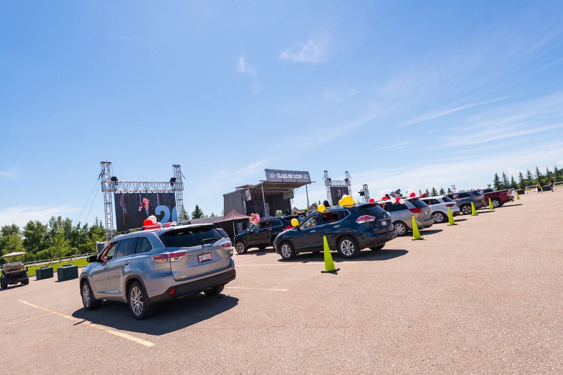 A row of cars are parked in a parking lot in front of a stage.