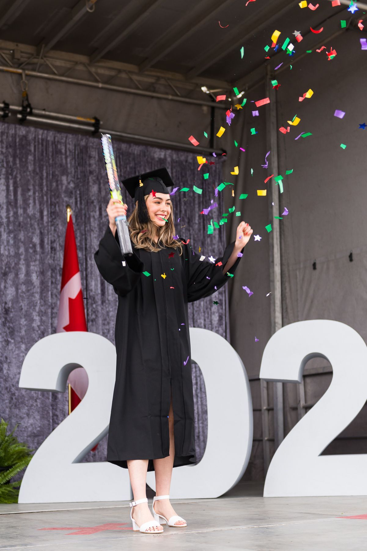 A woman in a graduation cap and gown is throwing confetti in the air.