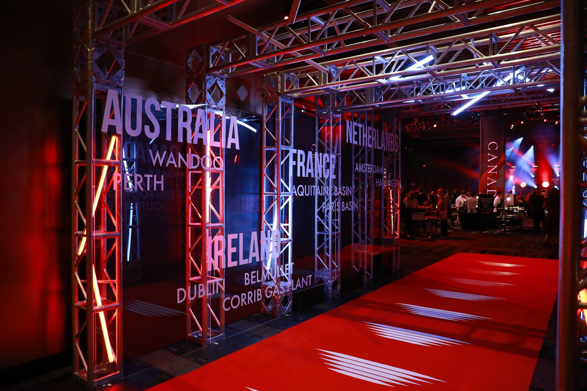 Red-carpet entrance with metal truss archway and illuminated country names, lit in red and blue