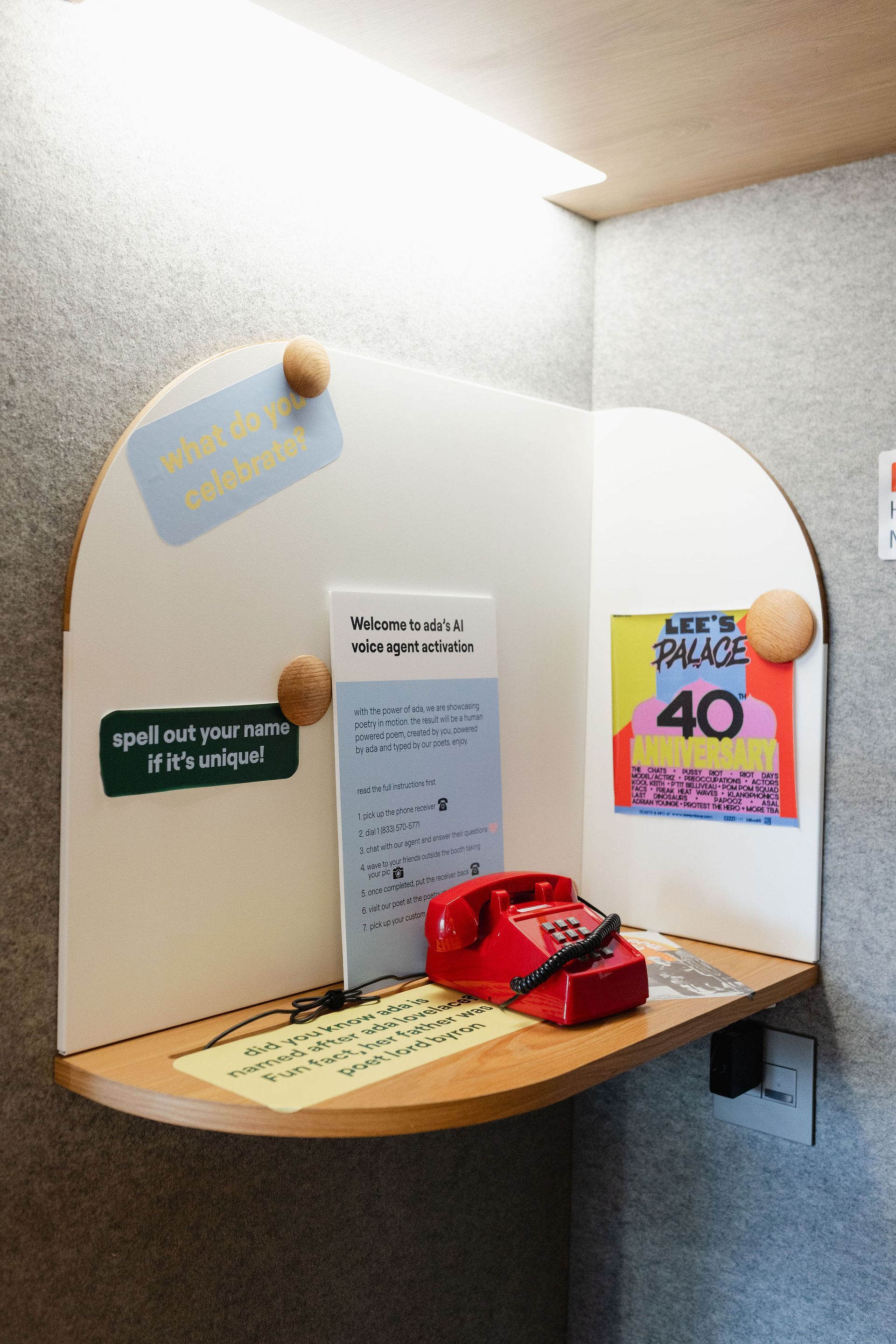 Red payphone in a booth with pinned notes, a poster, and light above.