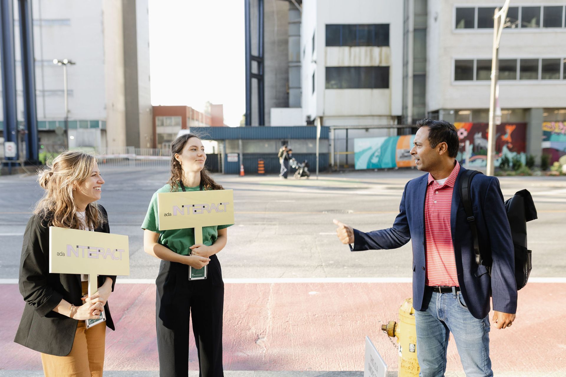 Three people with signs on a city street. Man gestures towards two women. Signs have text.